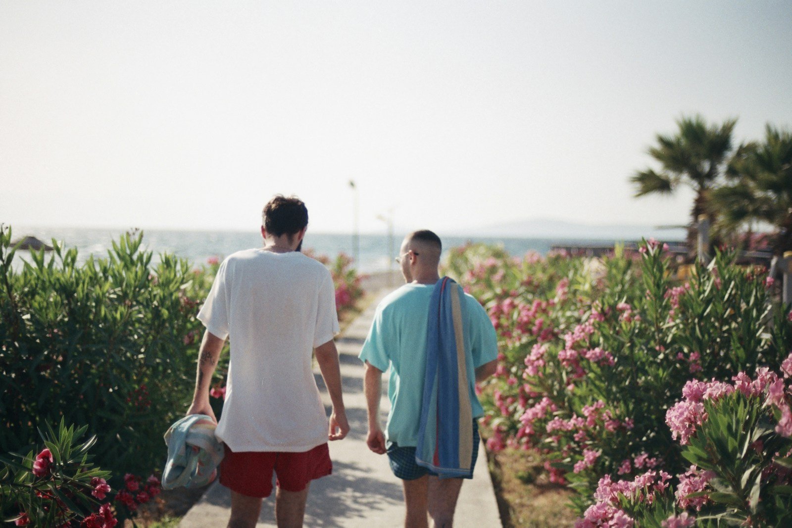 a couple of men walking down a sidewalk next to flowers